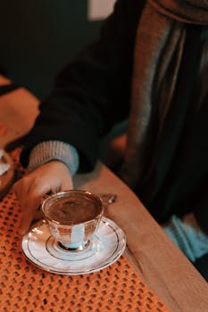 Cozy scene with hand holding traditional Turkish coffee in an elegant cup indoors.