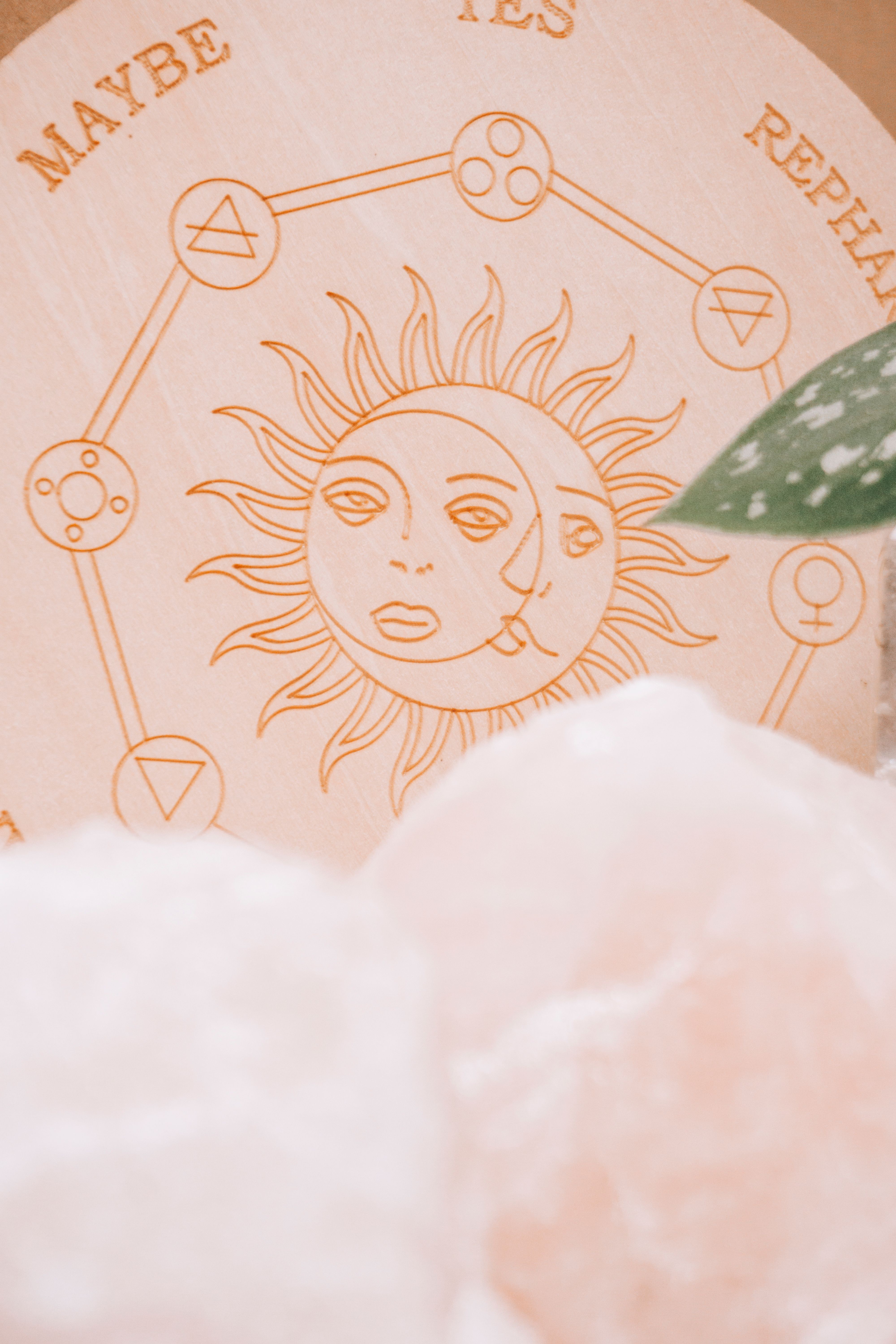 A mystical wooden sun and moon symbol surrounded by soft pink crystals, embodying spirituality and serenity.