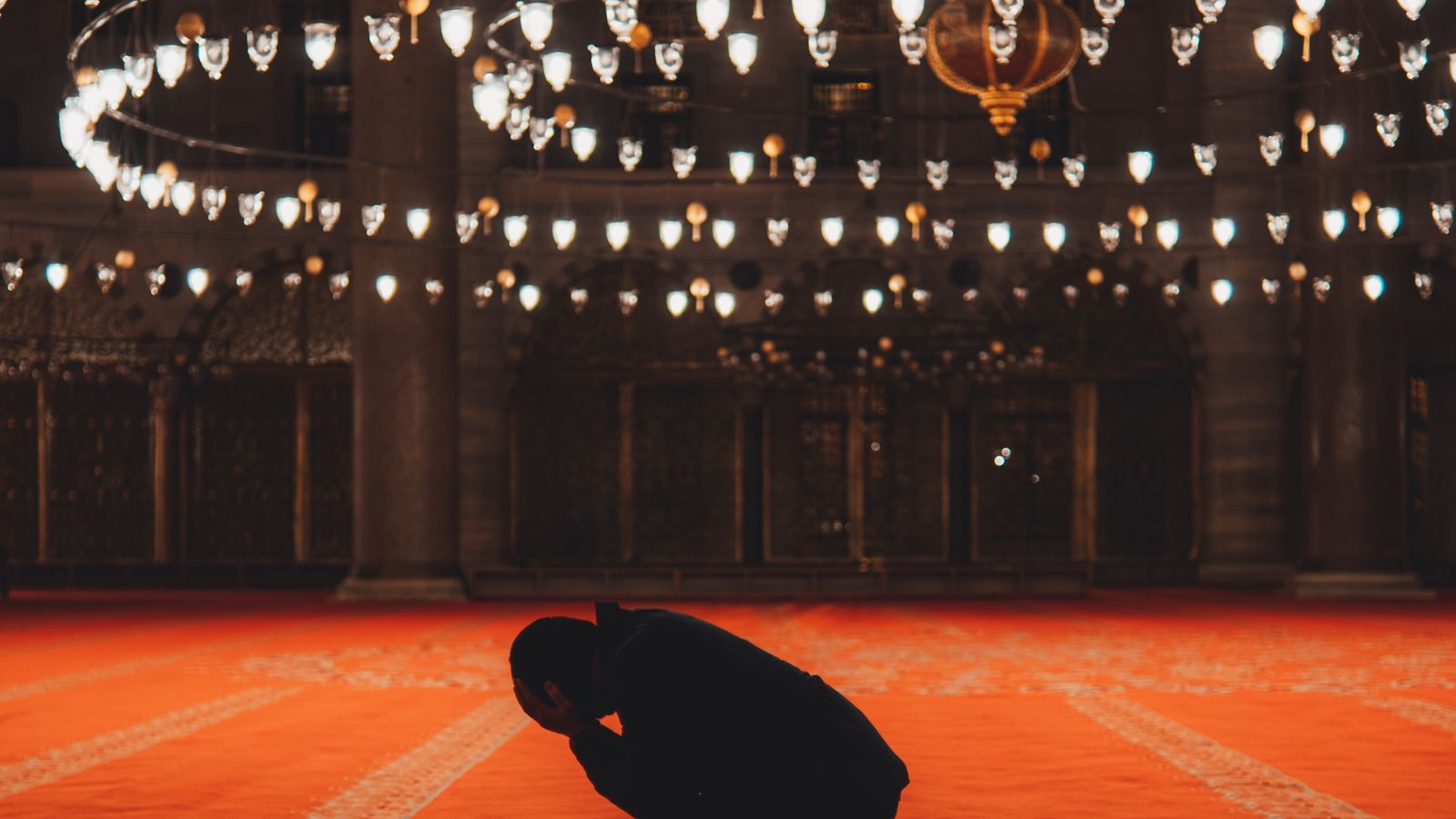 A Muslim man kneeling in silent prayer inside a beautifully illuminated mosque, the posture of humility before Allah in salatul tawbah