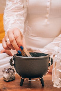 A hand places palo santo in a small cauldron surrounded by amethyst and crystals, enhancing relaxation and spirituality.