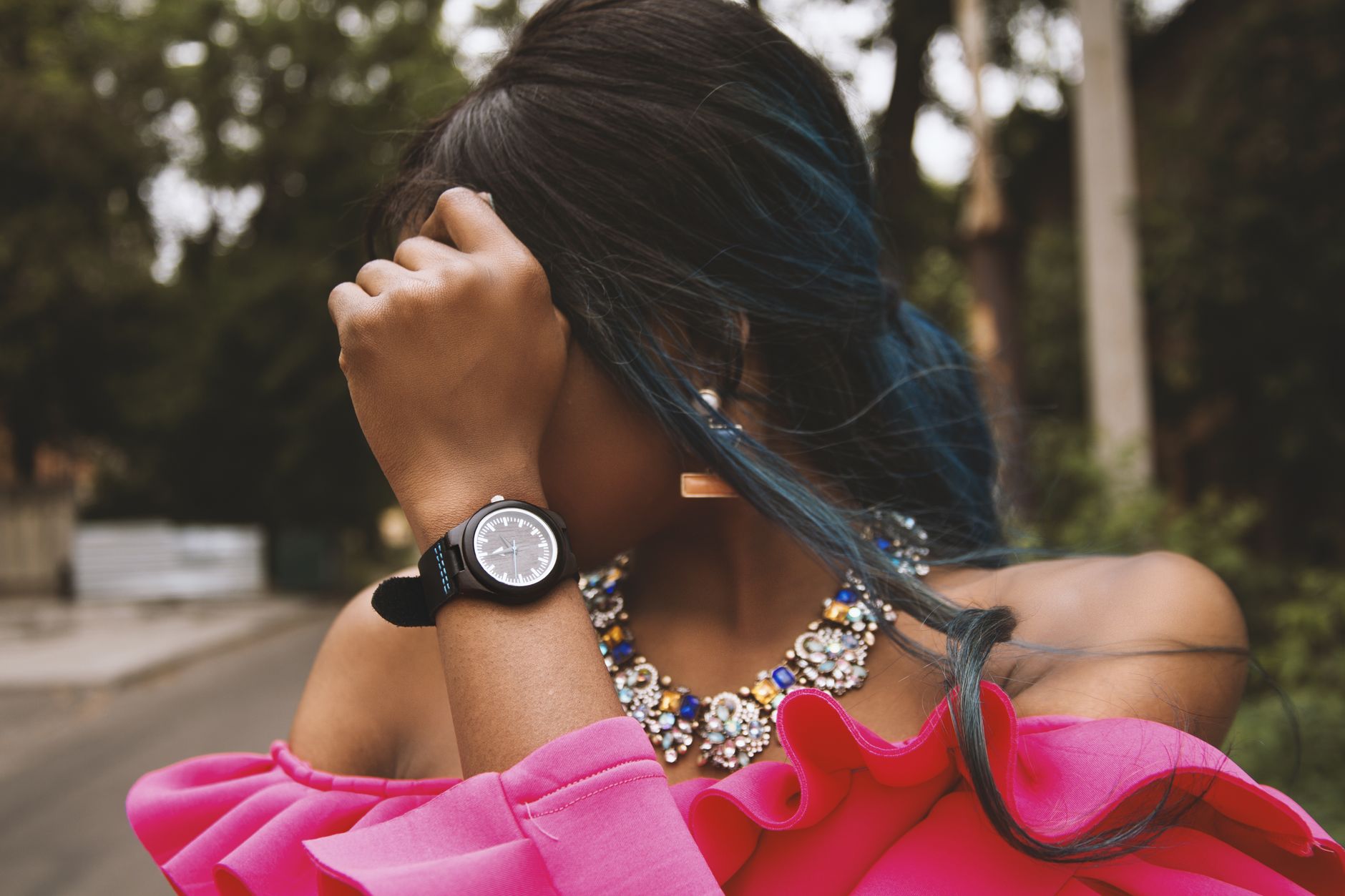 Fashionable woman in pink dress with necklace, adjusting hair outdoors.