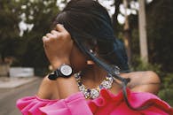 一位时尚女士穿着粉色连衣裙、戴着项链，在户外整理头发