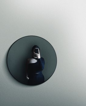 A stylish woman captures her reflection in a minimalist setting, showcasing fashion and elegance.