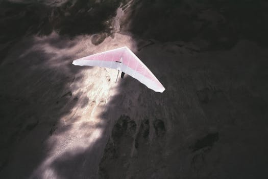 A scenic aerial shot of a hang glider soaring over a rugged landscape in daylight.