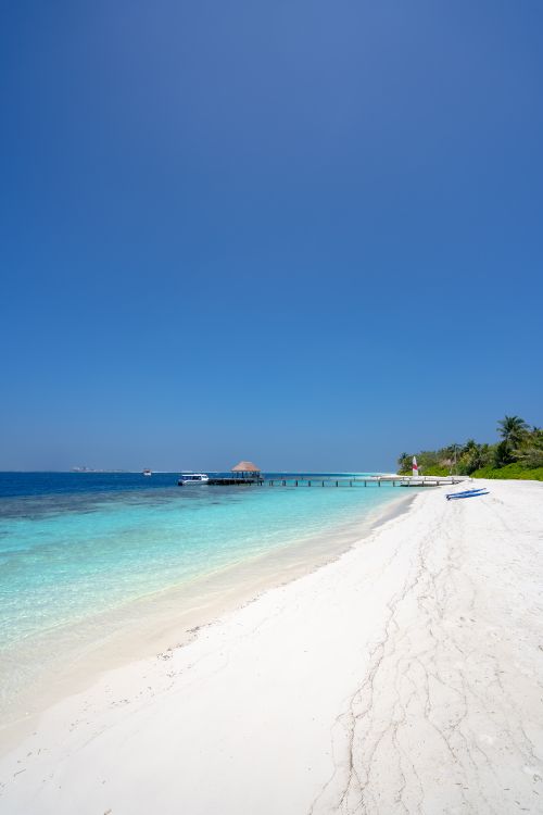 Free Serene tropical beach with pristine white sand and crystal-clear waters under a brilliant blue sky. Stock Photo