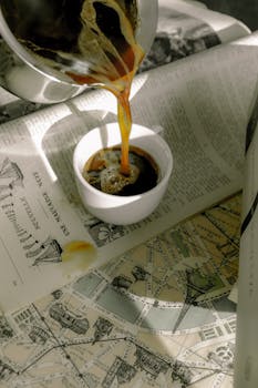 Close-up of Turkish coffee being poured into a cup over vintage Paris map, creating a rustic aesthetic.