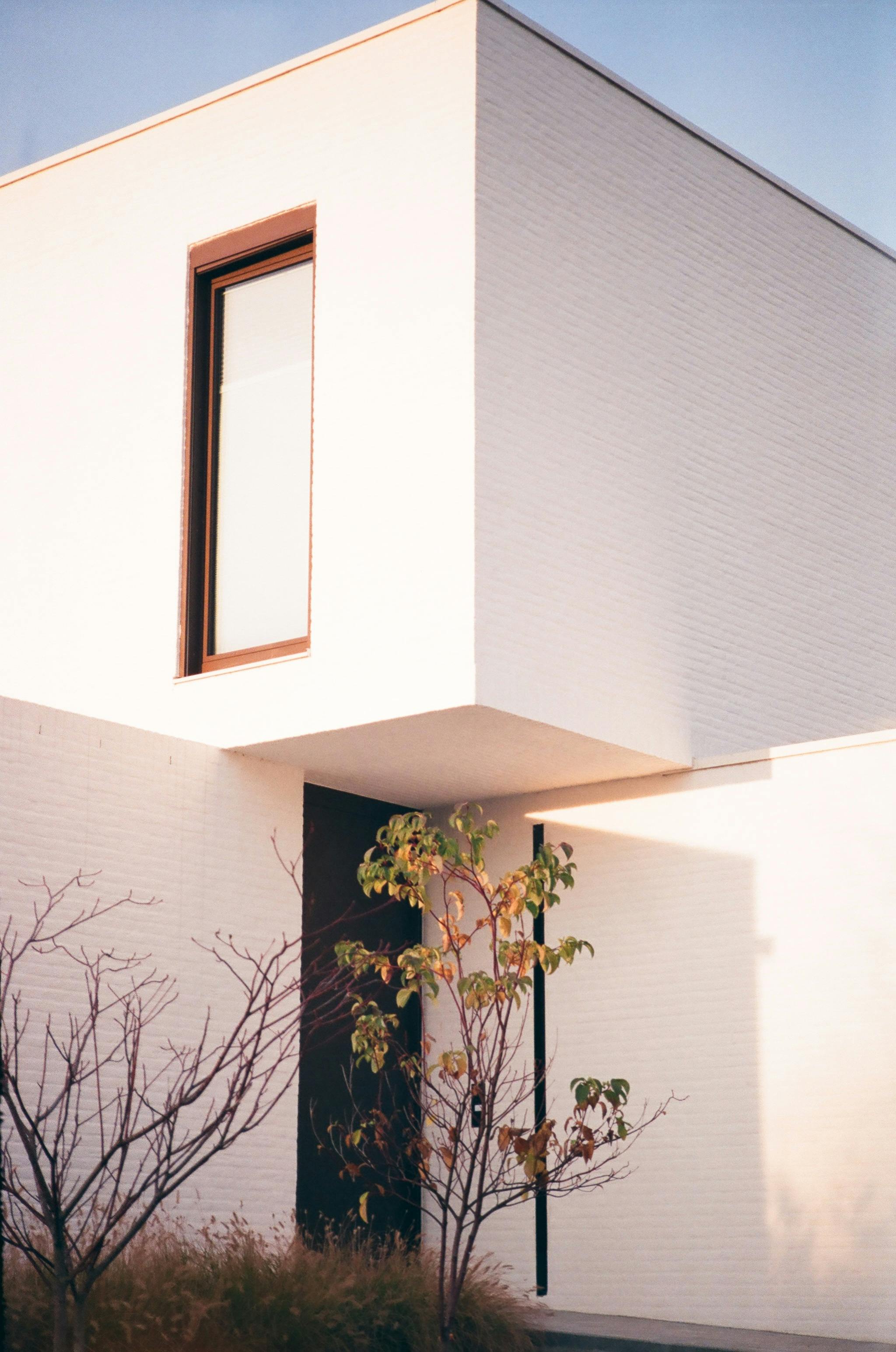 Explore this minimalist white brick house with large windows in a serene setting, reflecting modern design.