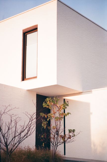 Explore this minimalist white brick house with large windows in a serene setting, reflecting modern design.