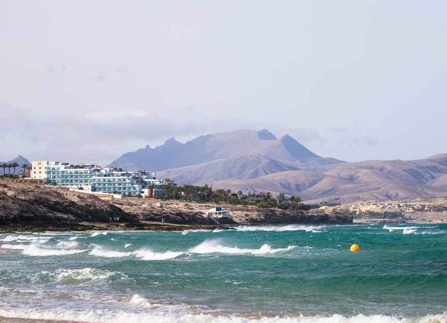 Scenic view of Fuerteventura coastline with waves and mountains in the background.