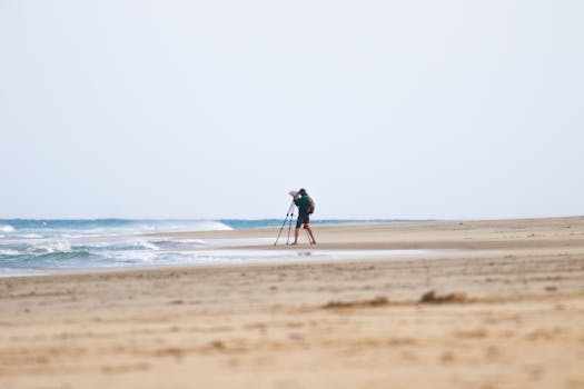 A photographer sets up a tripod on a secluded beach in Spain, capturing the ocean waves.