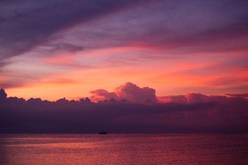Free A breathtaking sunset casting vivid colors over the calm sea with a distant boat silhouette. Stock Photo
