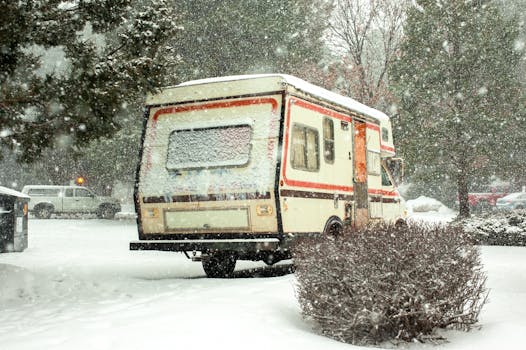 A campervan parked amidst heavy snowfall, surrounded by snow-covered trees and vehicles.