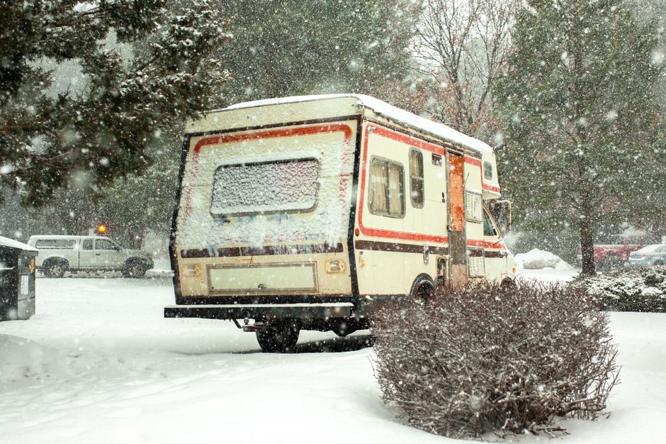A campervan parked amidst heavy snowfall, surrounded by snow-covered trees and vehicles.