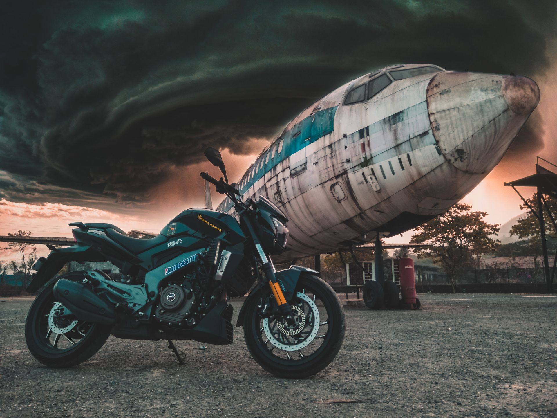 Motorcycle parked by an abandoned airplane under stormy skies, creating a dramatic scene.