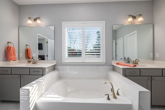 Elegant bathroom featuring a double vanity, bathtub, and natural light through window blinds.
