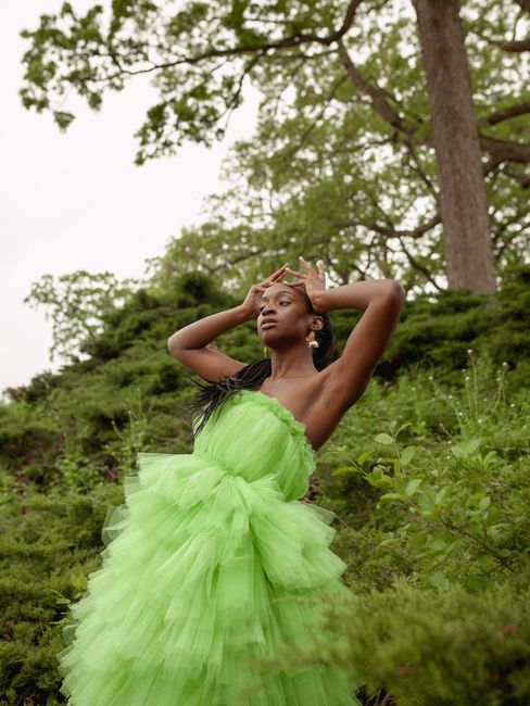 A stylish model poses gracefully in a vibrant green gown amidst lush greenery, showcasing fashion and nature.