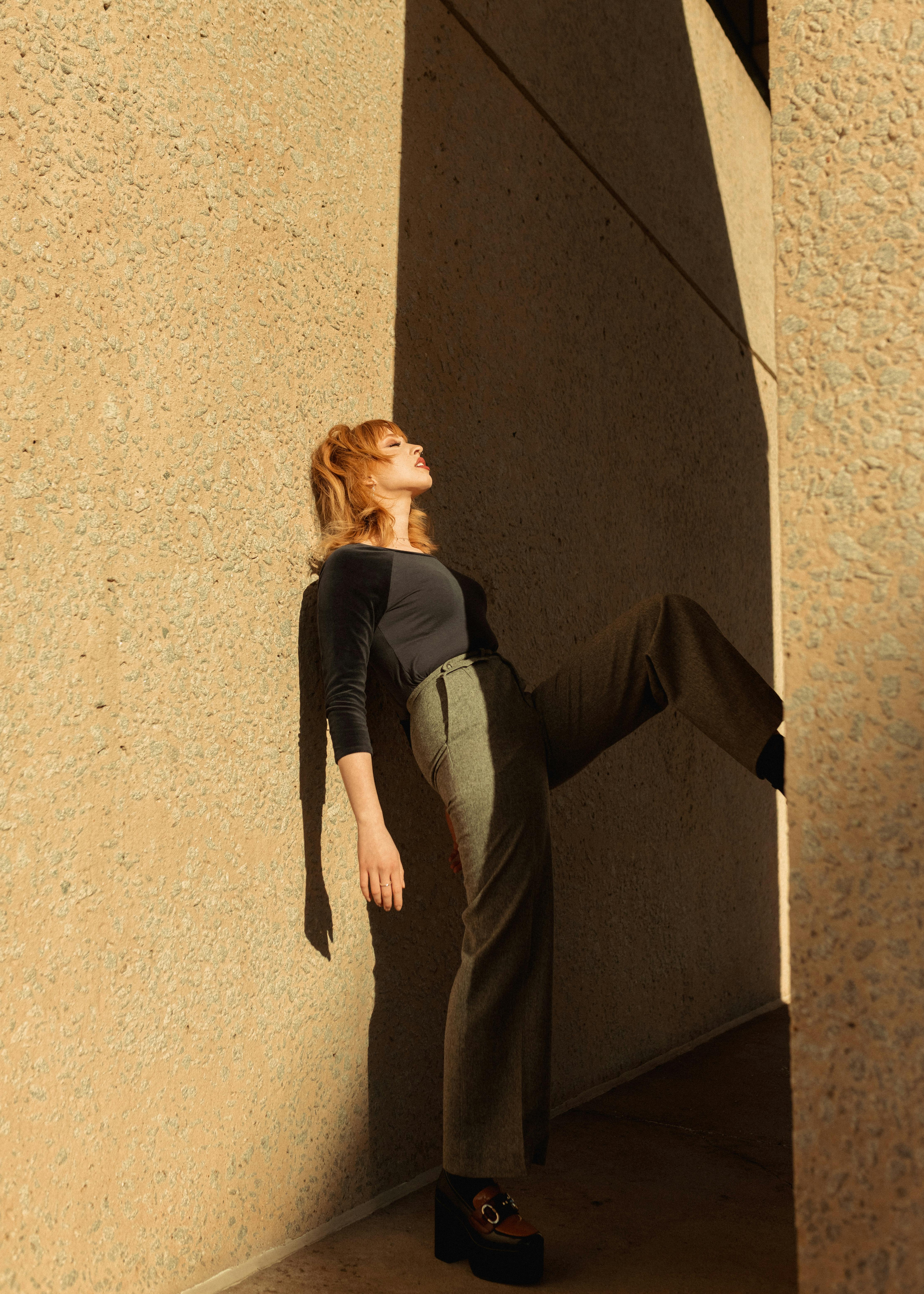Modern fashion shoot capturing a stylish woman leaning against textured wall.