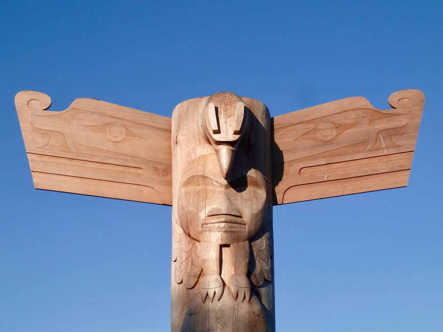 A traditional wooden totem with intricate carvings set against a clear blue sky.