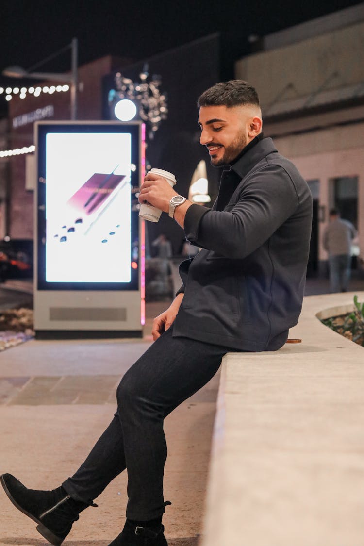 Smiling Man Sitting Outdoors Drinking Takeaway Coffee