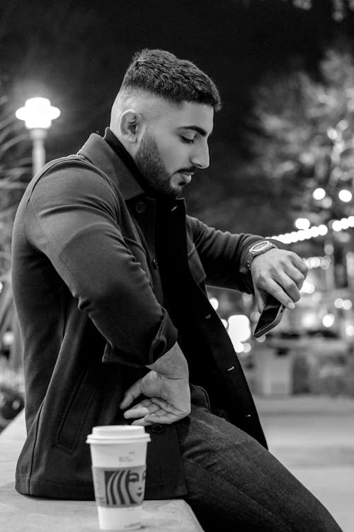 
A Grayscale of a Bearded Man in a Coat Looking at His Watch