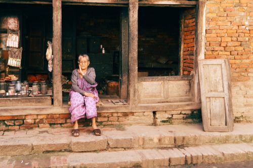 Free An elderly woman in traditional attire sits on a rustic verandah, embodying tranquility. Stock Photo