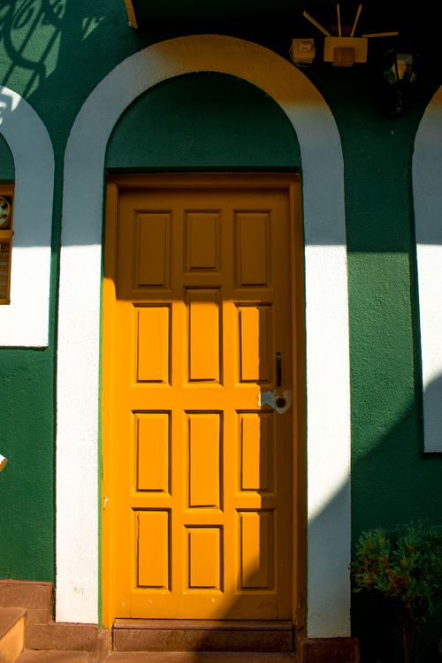 Free A vibrant yellow wooden door with an arched frame on a green wall, bathed in sunlight. Stock Photo