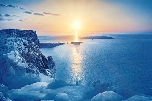 A breathtaking sunrise above a frozen coastline, illuminating the sea with warm colors.