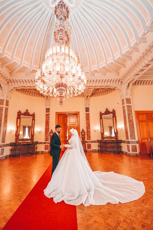 A Bride and Groom Standing Together on a Red Carpet while Holding Hands