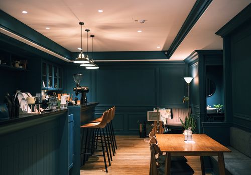 A beautifully lit, stylish modern coffee shop interior with wooden furniture and dark blue walls.