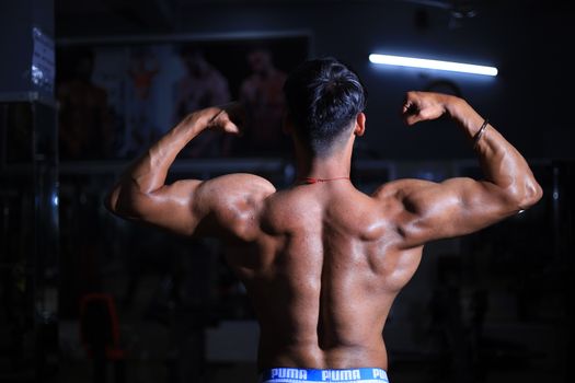 A muscular man flexes his back muscles in a dimly lit gym, showcasing strength and fitness.