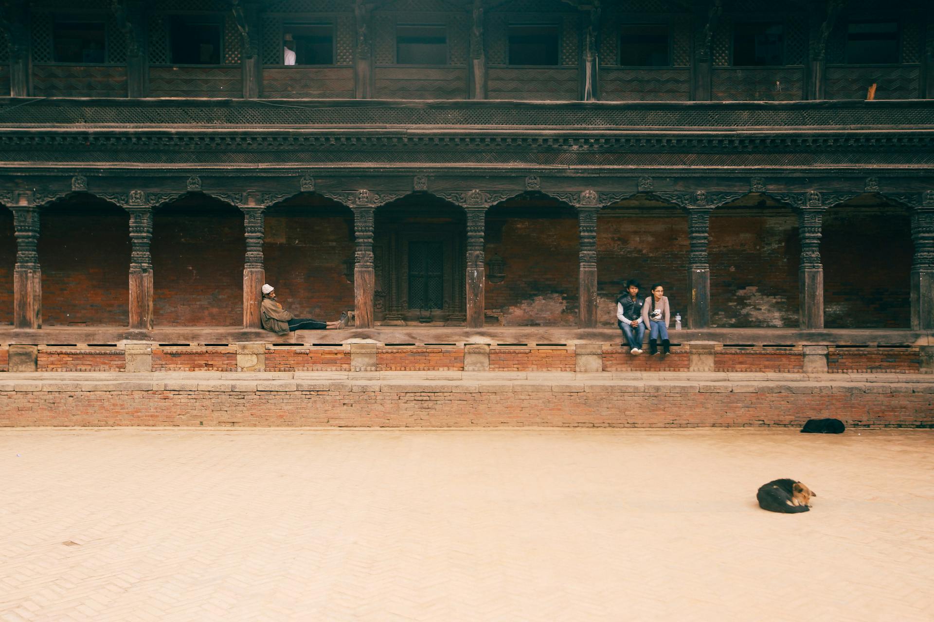 People Sitting in Temple Courtyard and Dog Sleeping