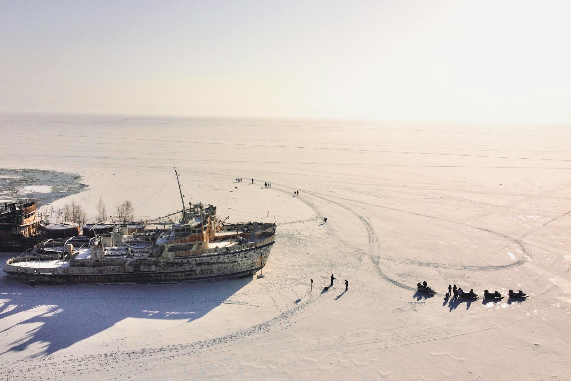 Dramatic aerial photo of an abandoned ship on a vast frozen lake during sunrise in winter.