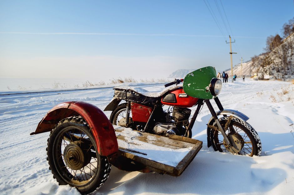 Red and green vintage motorcycle with sidecar parked on snowy road during winter.
