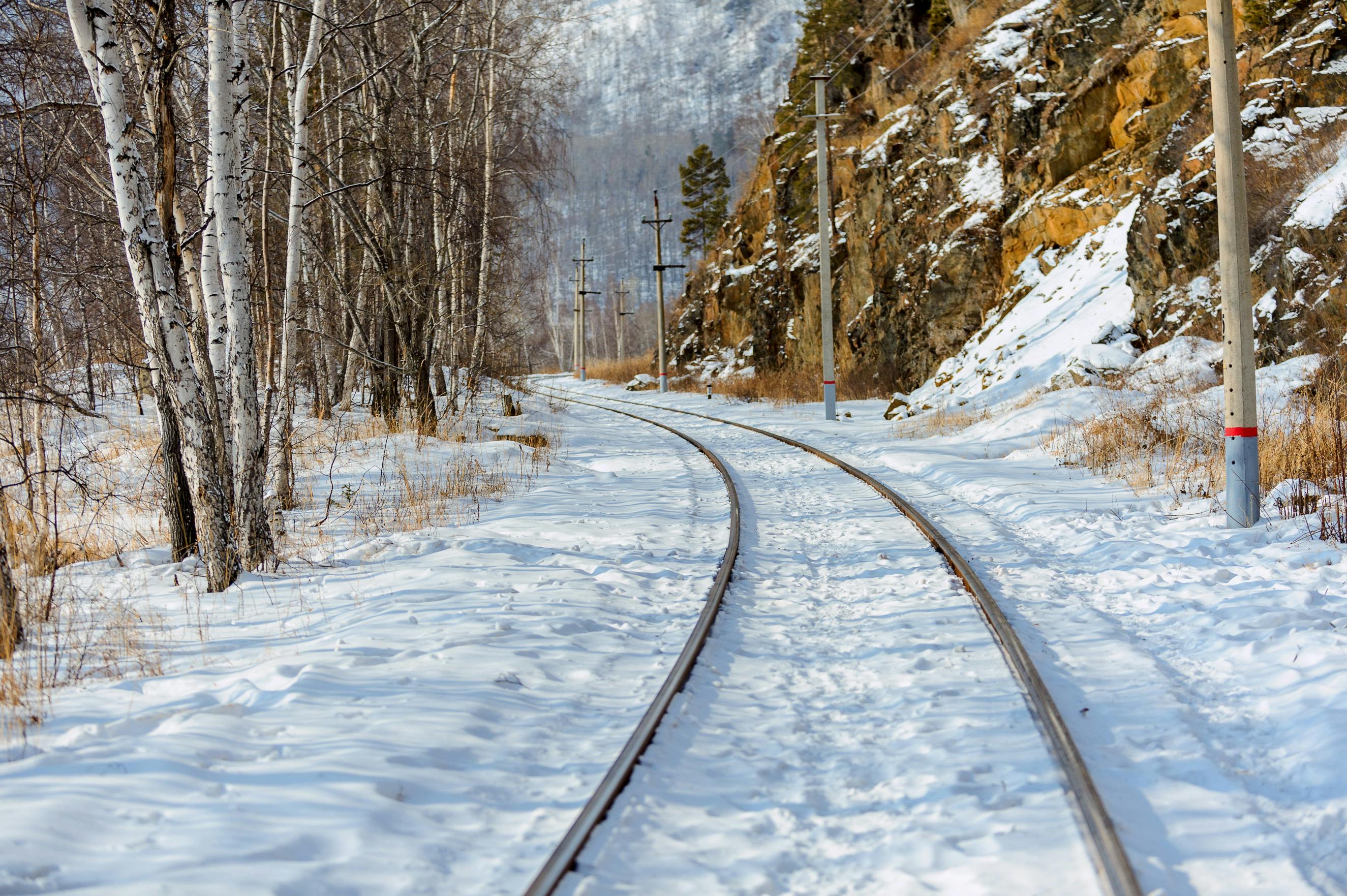 Serene snowy railway curving through a winter forest with birch trees and rocky hills.
