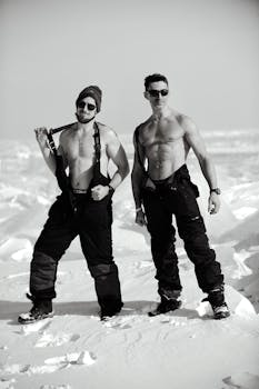 Two muscular men posing shirtless on a snowy landscape, showcasing strength against winter chill.