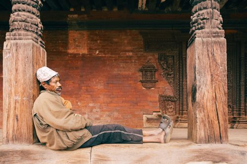 Free Elderly man peacefully napping against a wooden column in a temple with intricate carvings. Stock Photo