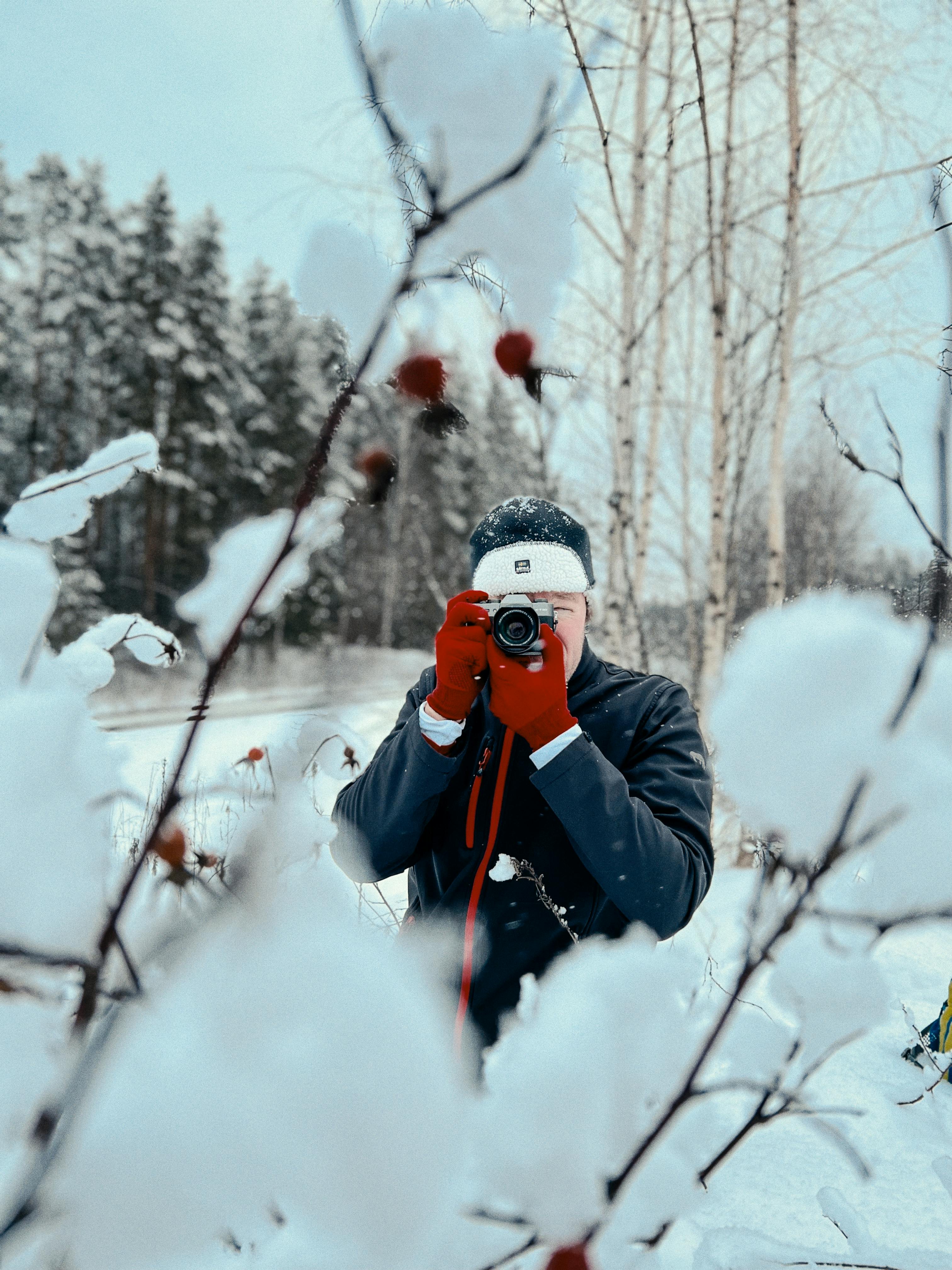 Photographer taking pictures in a snowy, wintry forest setting. Crisp, cold atmosphere reflects winter's beauty.
