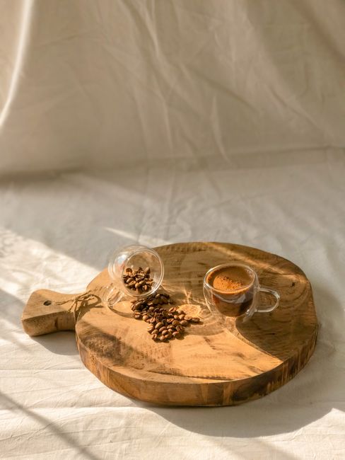 A cozy coffee scene featuring a glass cup of espresso and beans on a wooden board under warm sunlight.