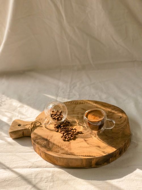 Free A cozy coffee scene featuring a glass cup of espresso and beans on a wooden board under warm sunlight. Stock Photo