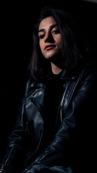 Dark, moody portrait of a woman wearing a black leather jacket in a studio.