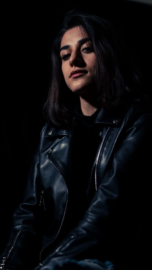 Free Dark, moody portrait of a woman wearing a black leather jacket in a studio. Stock Photo