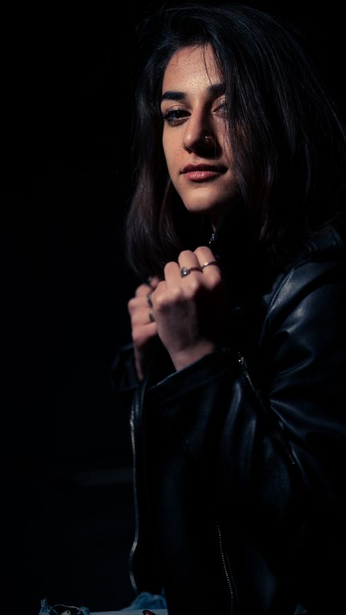 Free A moody close-up portrait of a woman in a black leather jacket with a dark background. Stock Photo
