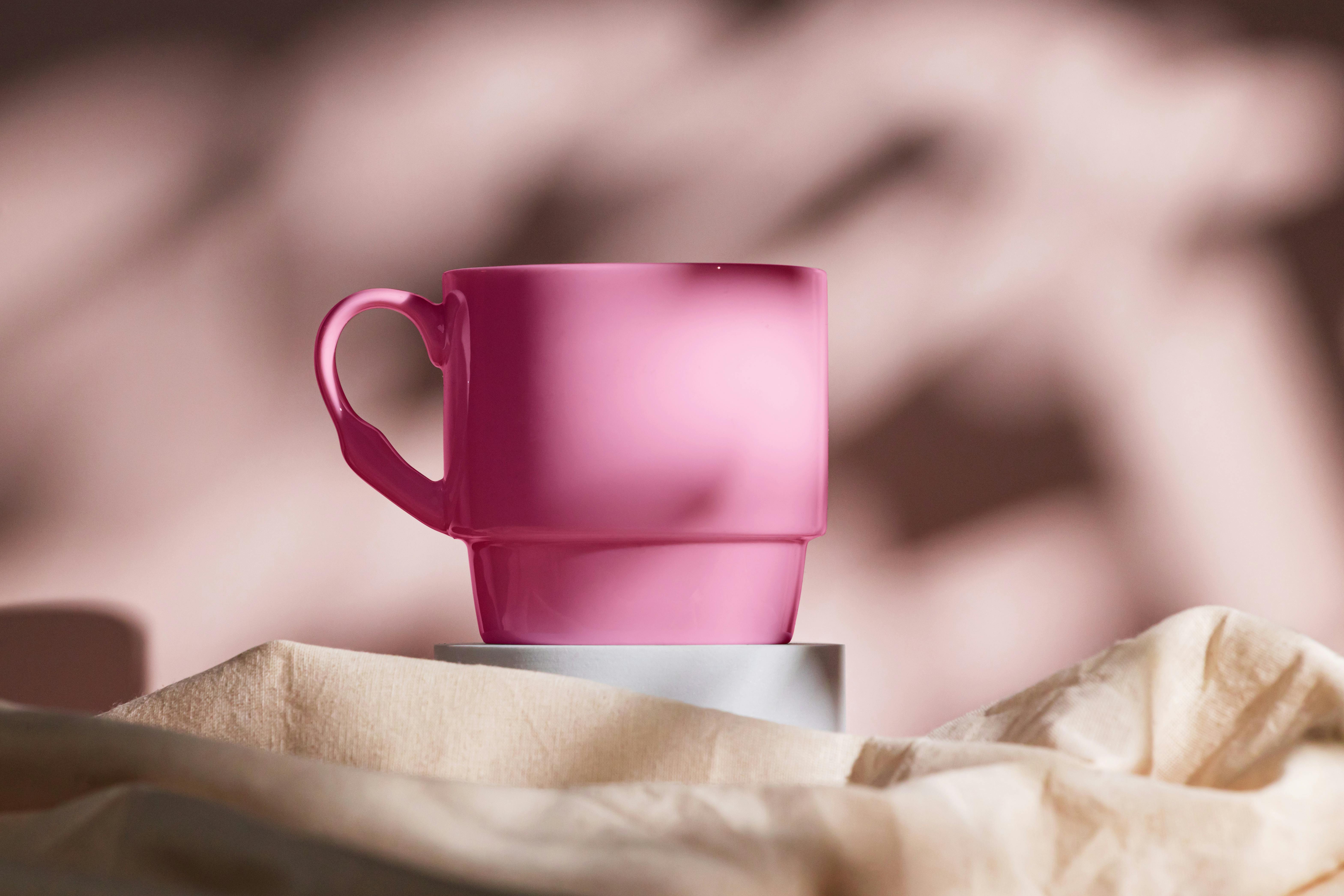 Elegant pink cup displayed on fabric with artistic shadows, conveying modern design.