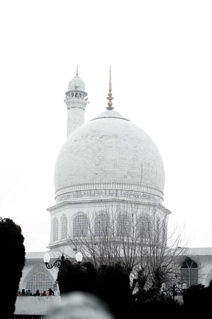 Stunning white marble dome and minaret of an Islamic shrine against a bright sky.