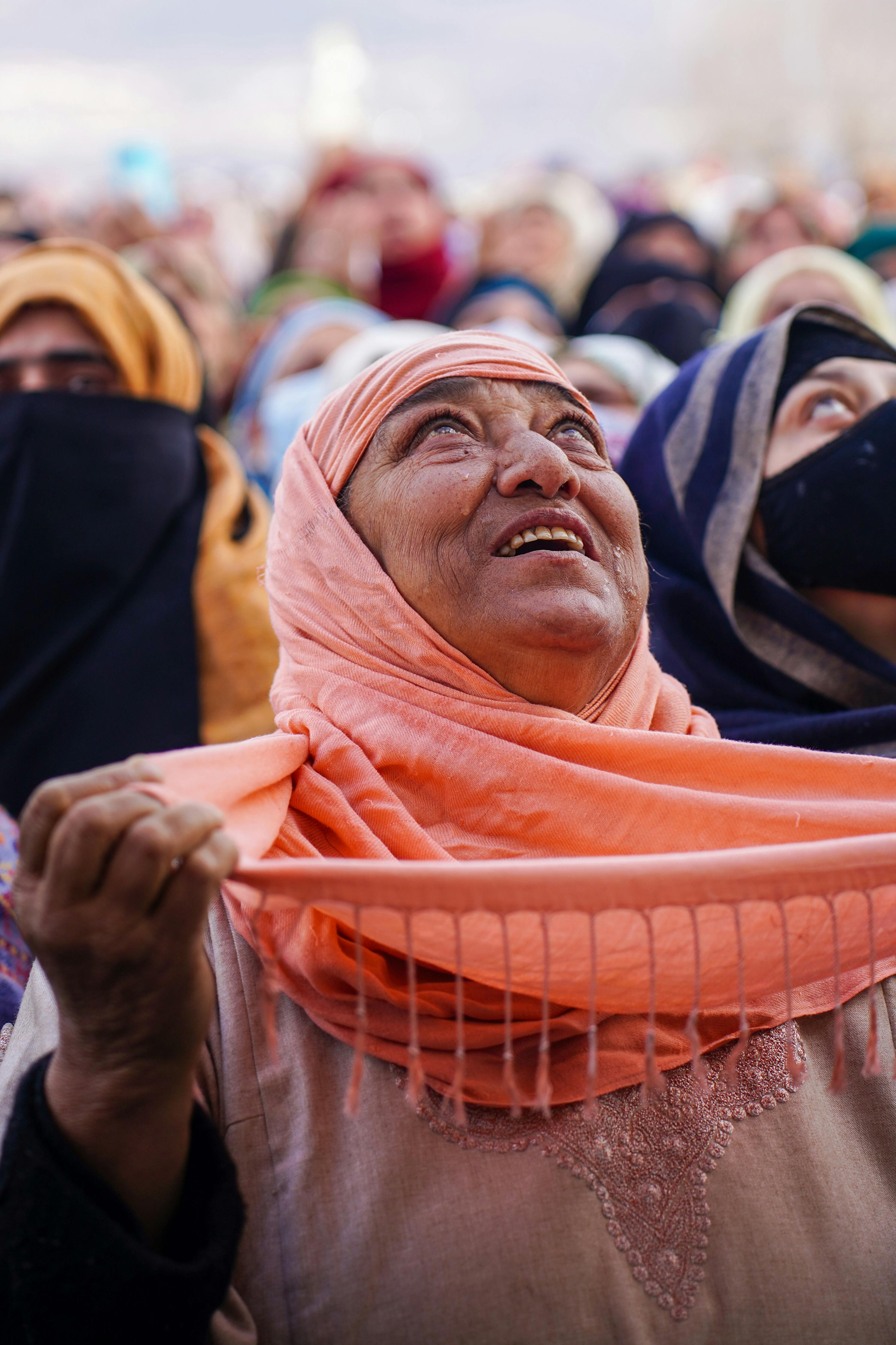 elderly person in orange hijab looking up while praying
