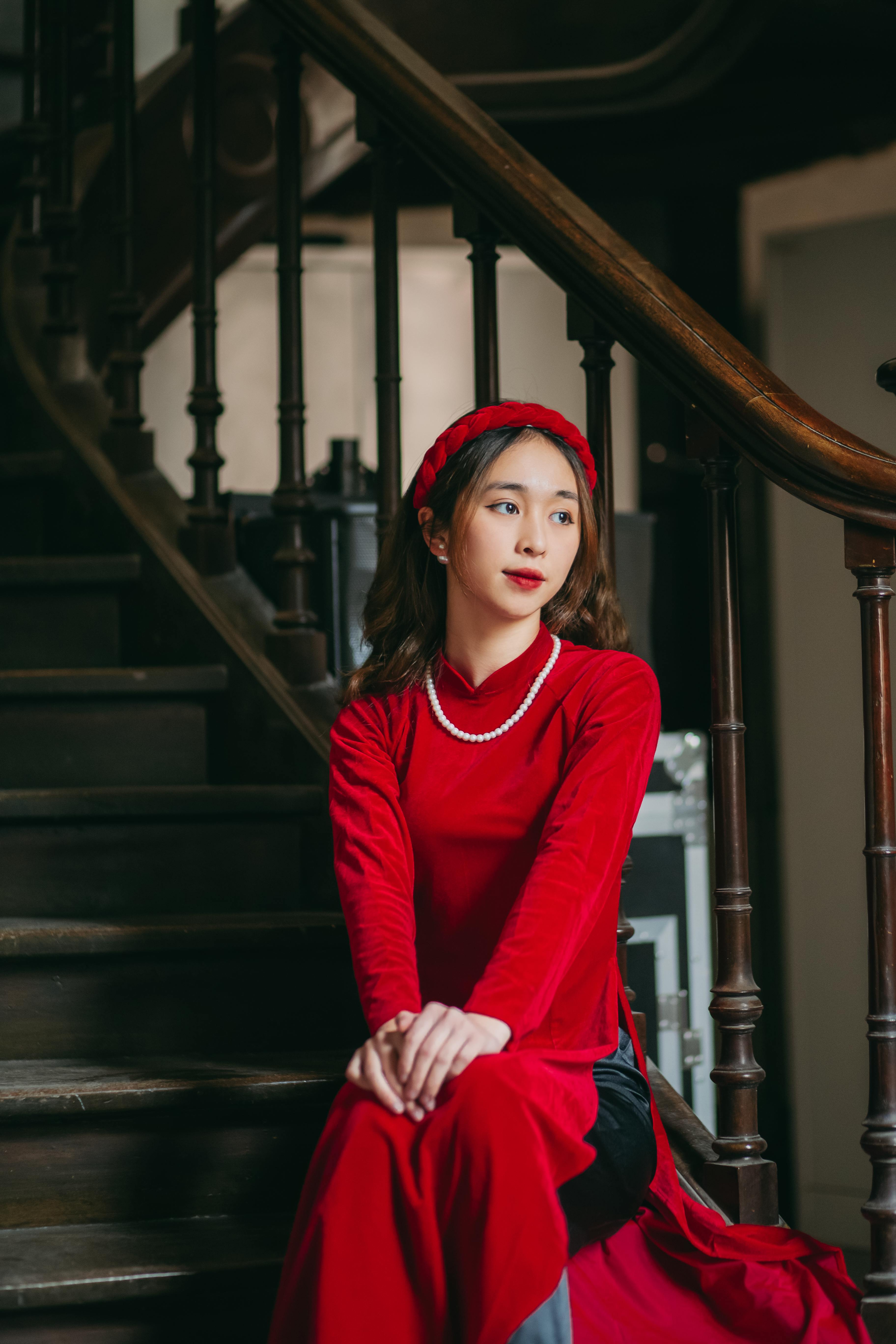 girl in red ao dai and pearl necklace sitting on stairs