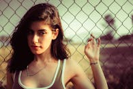 这幅迷人的肖像画，描绘了一位外表时尚的年轻女子，她正站在铁丝网栅栏旁