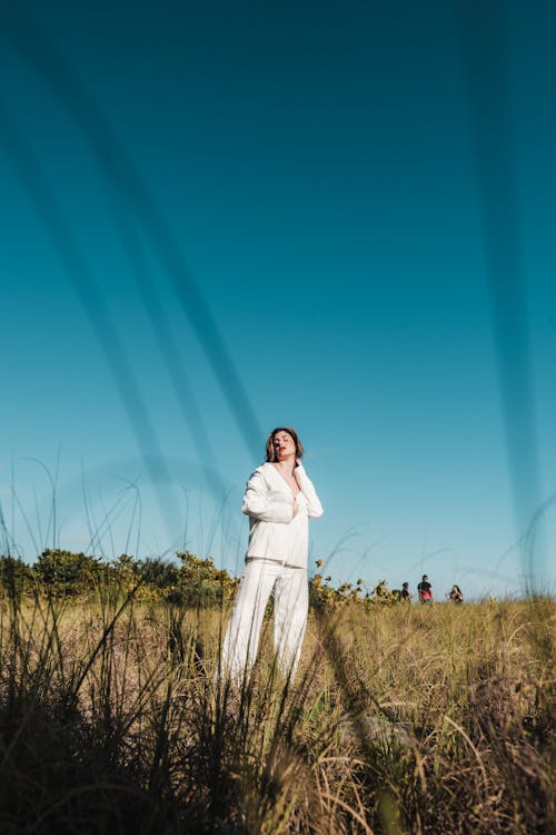 A Woman in White Long Sleeves and Pants Standing on Grass Field