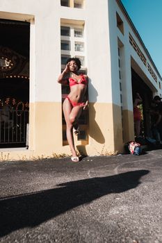 A woman in a red bikini poses confidently outdoors during a Miami photoshoot, bathed in bright sunlight.