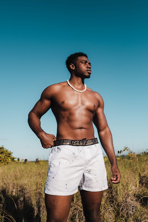 Topless Man in White Shorts Standing on Green Grass Field